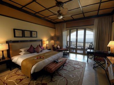 Modernes Schlafzimmer mit großem Bett, warmem Licht, Teppichboden und Balkon mit See- oder Meerblick.