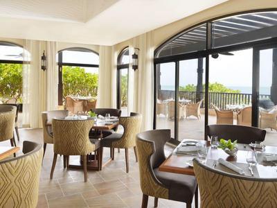 Helles Restaurant mit großen Fenstern, runden Tischen, bequemen Stühlen und Meerblick außen.