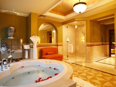 Luxuriöses Badezimmer mit großer Badewanne, rotem Sofa und goldfarbenen Wänden und Fliesen.