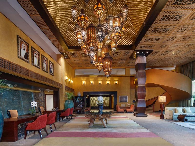 Luxuriöser Hotel-Lobbybereich mit goldener Decke, hängenden Laternen, roten Stühlen und Türmen aus Holz.