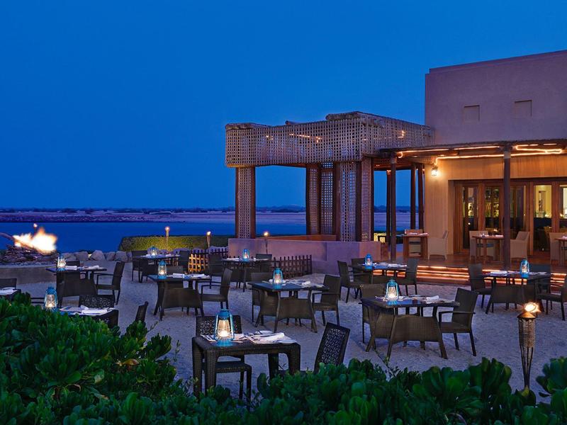 Moderner Außenbereich eines Restaurants mit Tischen und Stühlen bei Dämmerung am Meer.