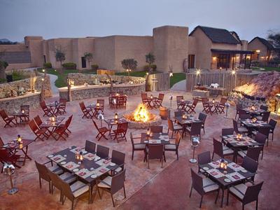 Freiluftrestaurant mit mehreren gedeckten Tischen und Feuerstelle bei Abenddämmerung.