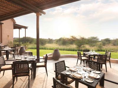 Terrasse mit gedeckten Tischen und Blick auf eine grüne Landschaft bei klarem Himmel.