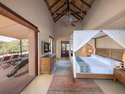 Luxuriöses Schlafzimmer mit Himmelbett und Terrasse in einer Safari-Lodge.