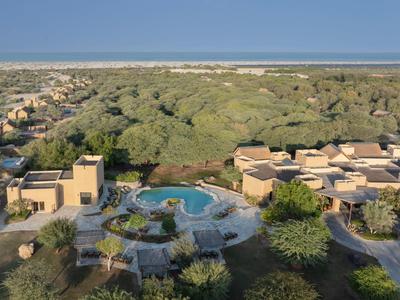Resort met zwembad omgeven door weelderig groen nabij een lang zandstrand.