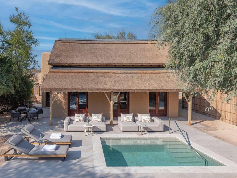 Moderner Pool mit Sonnenschirmen und Sitzbereich vor einem Haus mit Strohdach