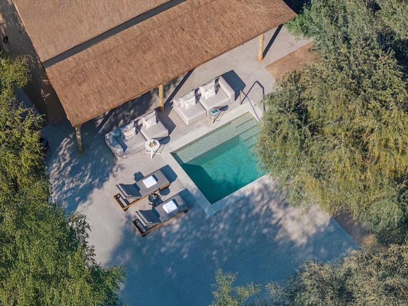 Luftaufnahme eines Pools mit Sonnenliegen und umliegenden Bäumen in einer Lodge.
