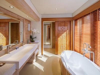Bright hotel bathroom with freestanding tub, double vanity, wooden blinds, and floral decor.