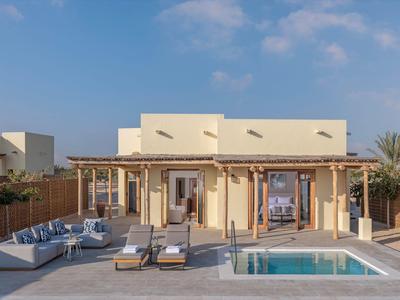 Moderner Bungalow mit privatem Pool, Sonnenliegen und Sitzbereich unter klarem Himmel.