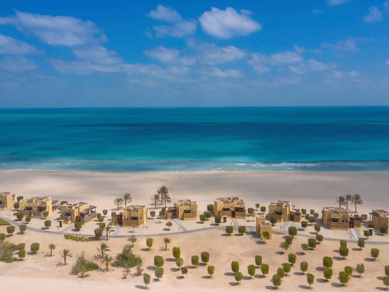 Aerial view of a tropical beach with umbrellas and lounge chairs arranged in rows.