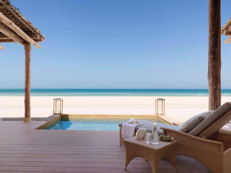 Relaxing beach villa with pool overlooking the ocean and sandy shore under clear sky.