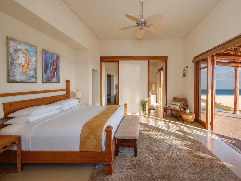 Spacious bedroom with king bed, artwork, fan, and sliding doors opening to ocean view patio.