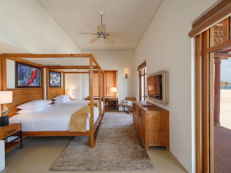 Spacious bedroom with a four-poster bed, wooden furniture, and a view of the beach.