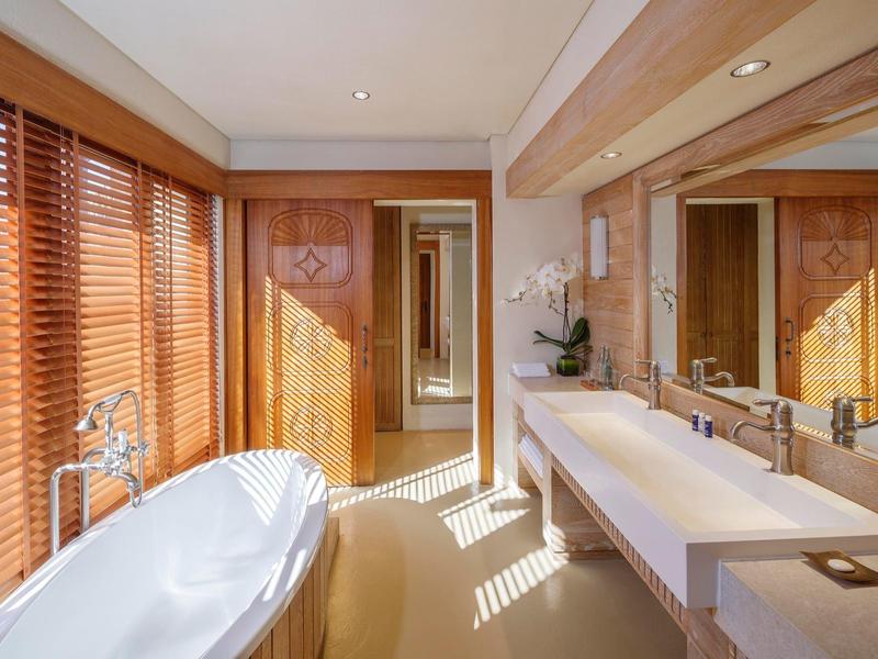 Bright hotel bathroom with large bathtub, double sink, wooden blinds, and modern fixtures.