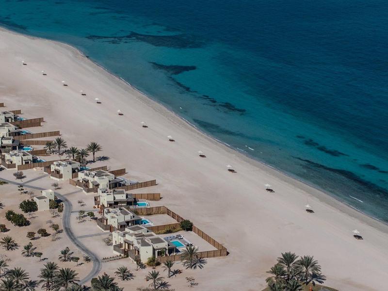 Aerial view of a quiet sandy beach with few buildings and clear blue sea.