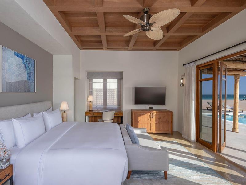 Modern hotel room with large bed, wooden ceiling, and sea view through sliding doors.