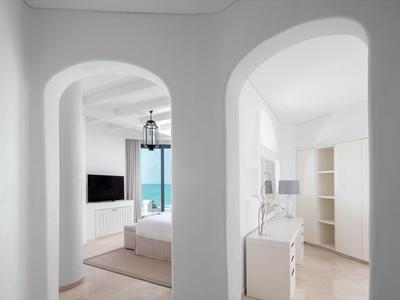 White minimalist hotel interior with sea view through rounded arch doorway.