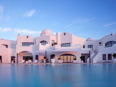 White modern hotel with smooth curves and large pool in foreground at sunset.