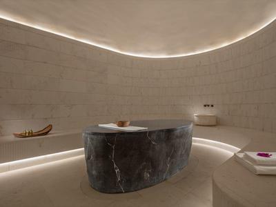 A modern spa room with a round marble tub and soft indirect lighting.