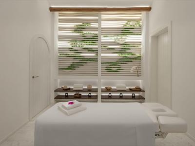 Bright massage room with table, towels, and decorative plants behind blinds.