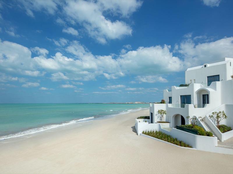 White houses by a calm sandy beach under blue sky with clouds.