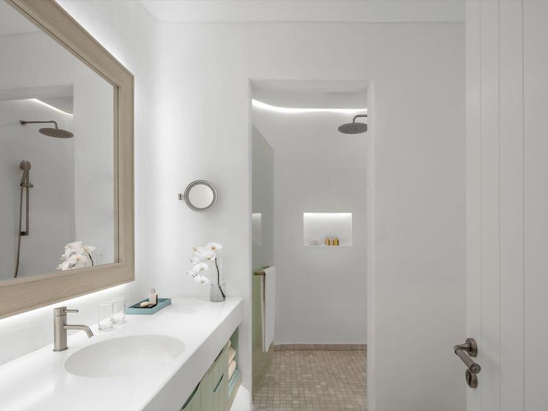 Modern hotel bathroom with double sinks and walk-in shower in neutral tones.