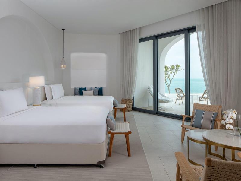 Bright hotel room with two beds and balcony overlooking the sea.