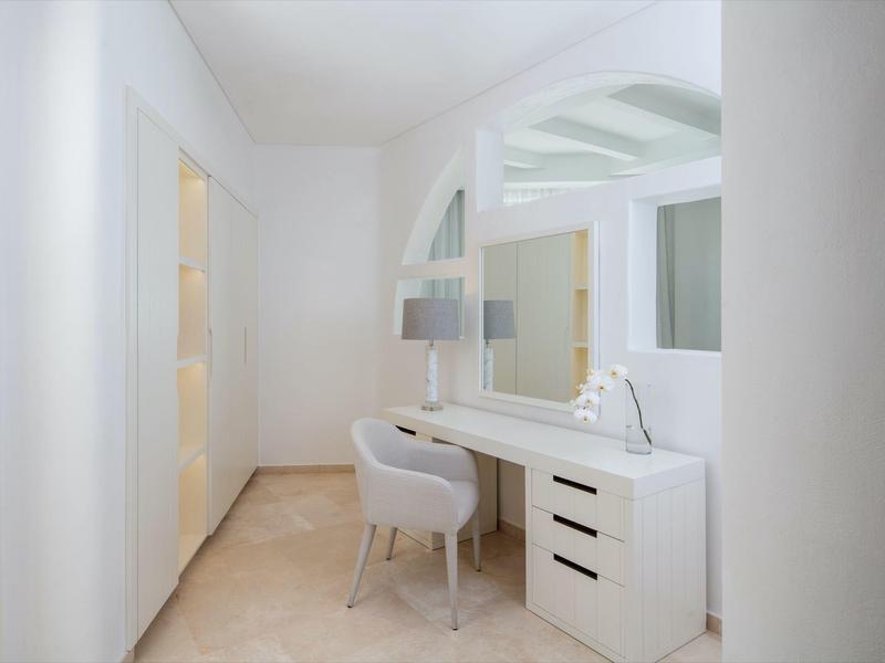 Bright vanity table with large mirror and comfortable white chair in a light room.
