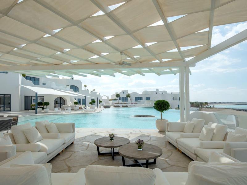 Luxury lounge with white sofas overlooking the pool and sea under a sunshade.