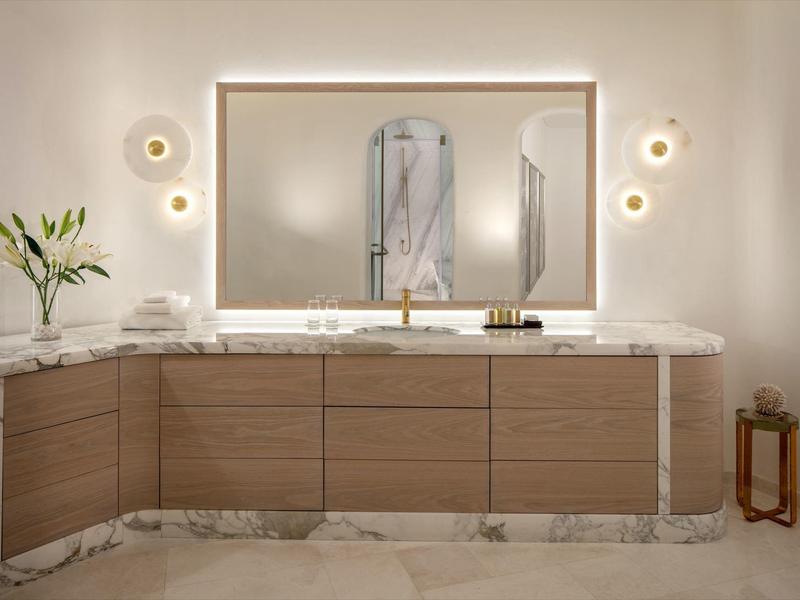 Modern bathroom vanity with wooden fronts, large mirror, and gold wall lights.
