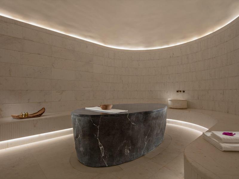 A modern spa room with a round marble tub and soft indirect lighting.