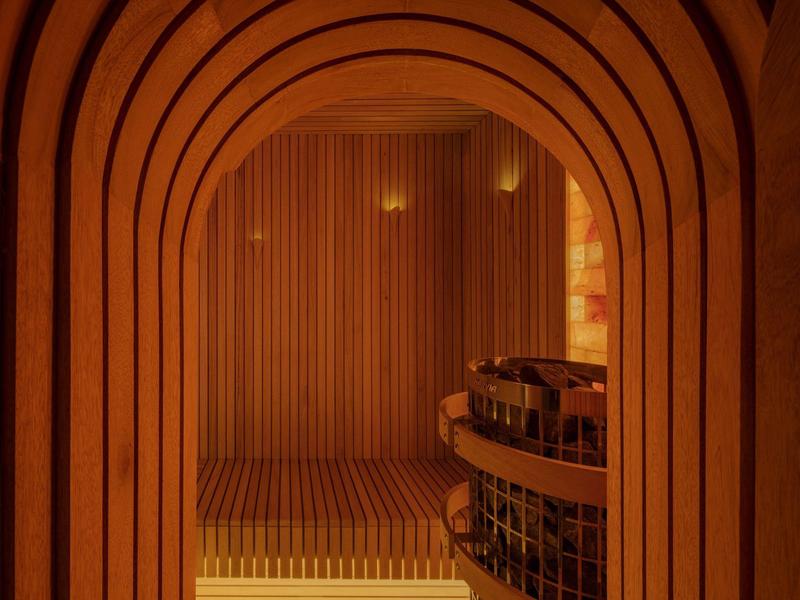 View through arched wooden frame into cozy sauna room with benches and lighting.