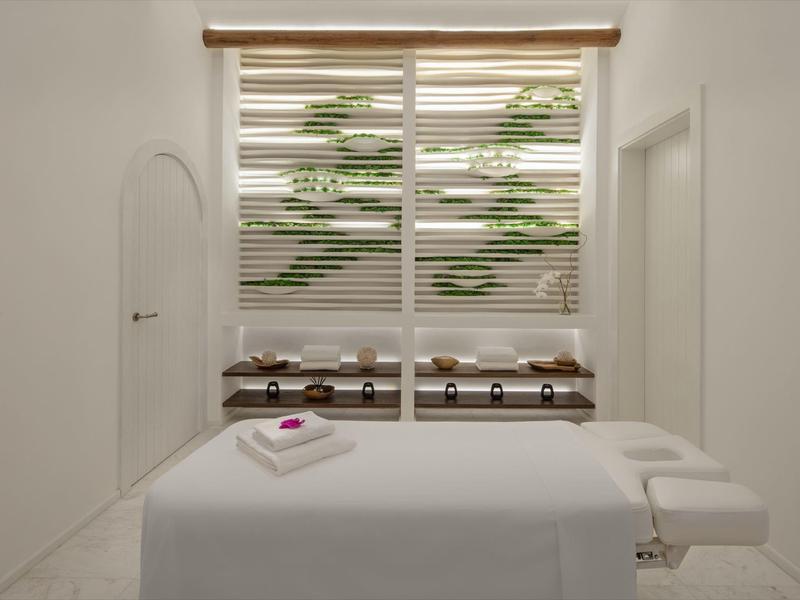 Bright massage room with table, towels, and decorative plants behind blinds.