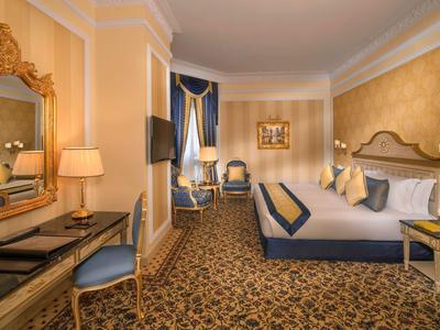 Elegantes Hotelzimmer mit großem Bett, goldener Wand, Teppichboden und Sitzbereich.