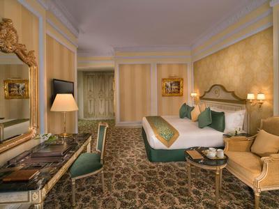 Elegantes Hotelzimmer mit großem Bett, Sesseln und einem Schreibtisch in warmen Farbtönen.