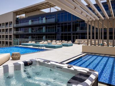 Moderner Hotelpoolbereich mit Außenwhirlpool, Liegestühlen und Glasfassade unter Sonnenschutz.