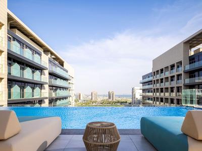 Infinity-Pool zwischen zwei modernen Hotelgebäuden mit Blick auf die Stadt unter blauem Himmel.