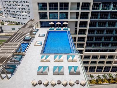 Dachterrasse mit rechteckigem Pool, Liegestühlen mit Schirmen und modernen Gebäuden im Hintergrund.