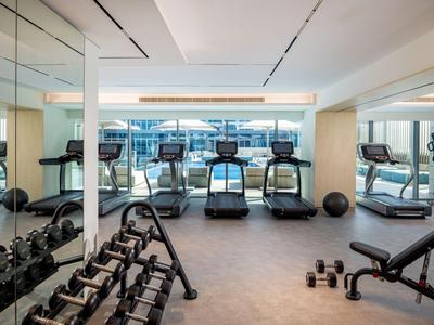 Heller Fitnessraum mit Laufbändern, Hanteln und Spiegelwand in einem Hotel.