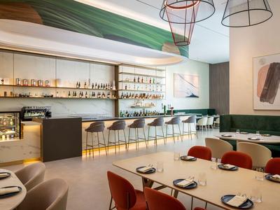 Modernes Hotelrestaurant mit langen Bartresen, roten Stühlen und stilvoller Beleuchtung.