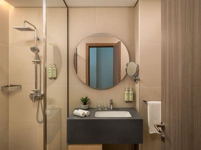 Moderner Hotelbadezimmer mit runden Spiegel, Waschbecken und Duschkabine in neutralen Farben.