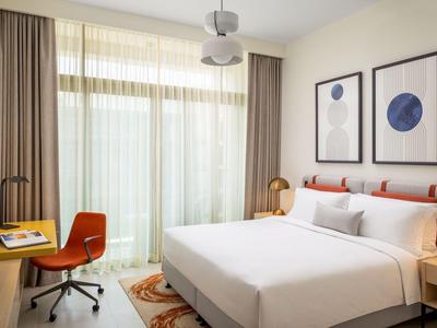 Modernes Hotelzimmer mit großem Bett, Schreibtisch und bodentiefen Fenstern.