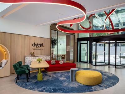 Moderner Hotellobby mit bunten Möbeln, rundem Teppich und großen Fensterfronten.