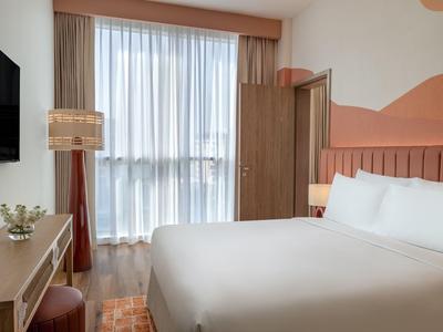 Modernes Hotelzimmer mit Doppelbett, Schreibtisch und großem Fenster mit Vorhängen.