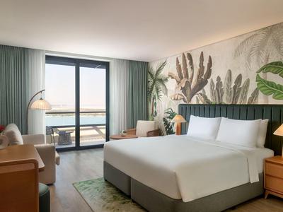 Modernes Hotelzimmer mit Kingsize-Bett, Pflanzenwanddekor und Balkon mit Meerblick.