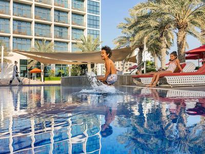 Kinder spielen am Pool eines Hotels mit Palmen im Hintergrund.