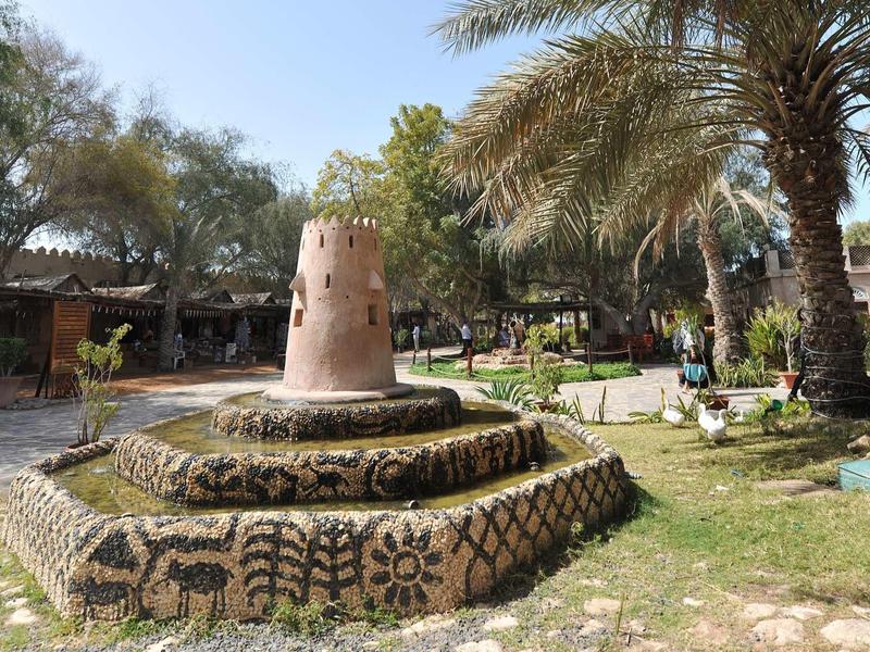 A round, multi-tiered stone structure with decorations in a tropical garden with palm trees.