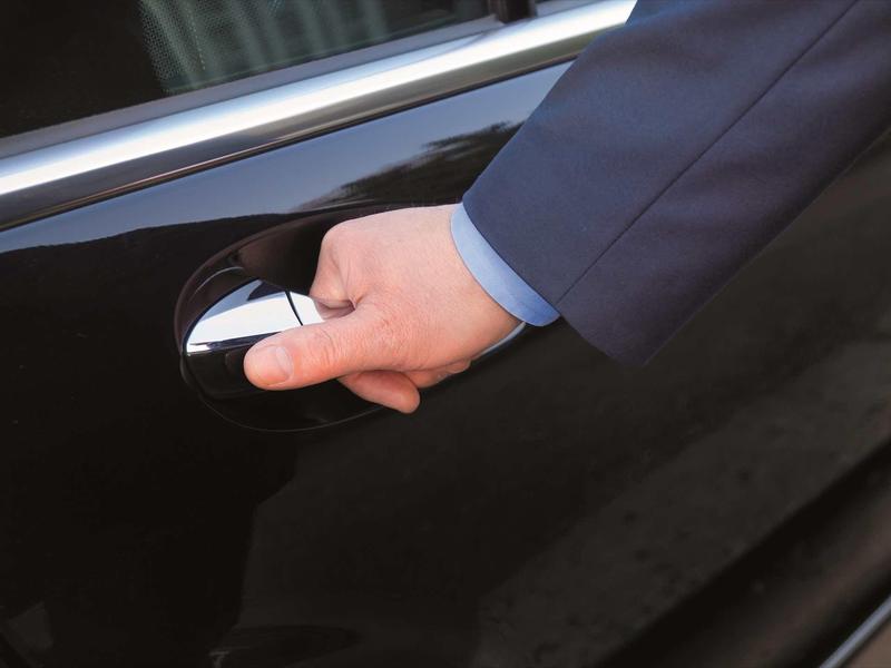 A hand in a suit opens the door of a black car.