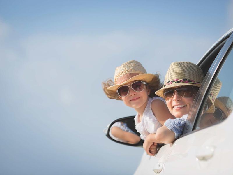 A couple leans out of car windows wearing sun hats and sunglasses under a clear sky.