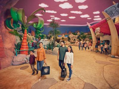 Una famiglia in abiti casual passeggia in un parco a tema con decorazioni colorate e altri visitatori.